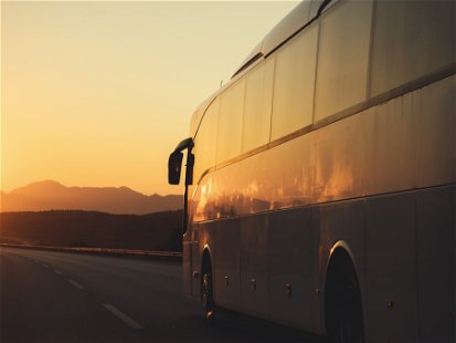 White bus driving on road towards the setting sun