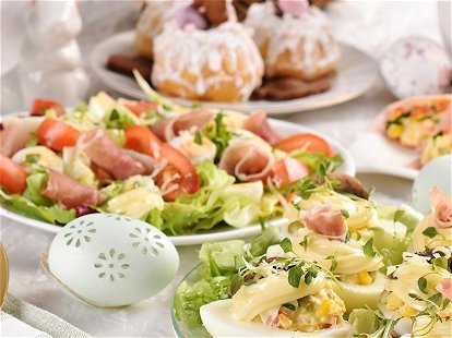Easter breakfast with fresh salad with quail eggs, stuffed eggs with mayonnaise, ham rolls and traditional pastries on festive table