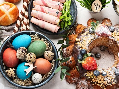 Traditional Easter dinner or  brunch with ham, colored eggs, hot cross buns, cake and vegetables. Easter meal dishes with holday decorations. Top view, copy space, panorama, banner