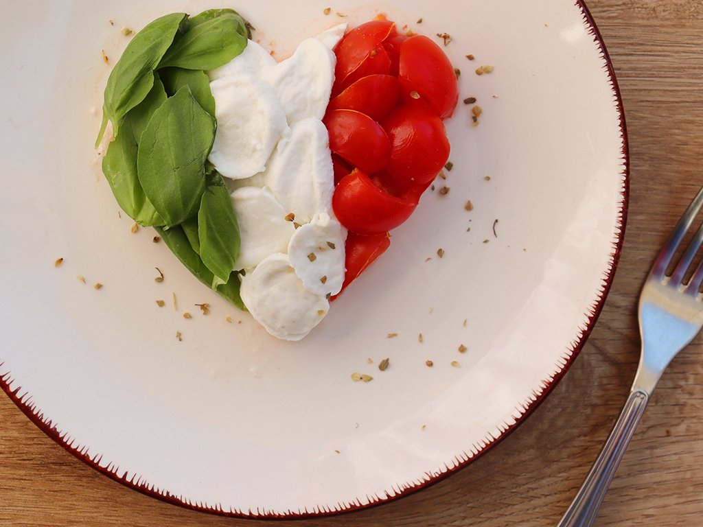 Heart shaped Italian Caprese Salad arranged by Italian basil,buffalo mozzarella and tomatoes look like Italian Flag on plate with wooden table background.Love Italian food concept for Valentine day