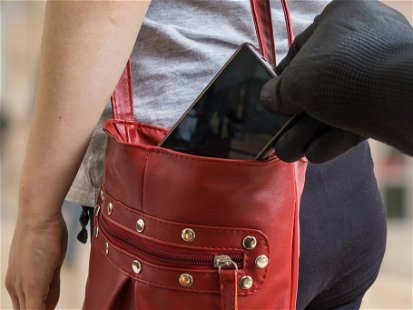 Pickpocket thief is stealing smartphone from red handbag.