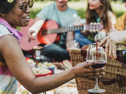 Group of friends making picnic lunch and drinking wine outdoor - Young people having fun while eating and relaxing - Focus on african girl face - Youth lifestyle, holidays and friendship concept