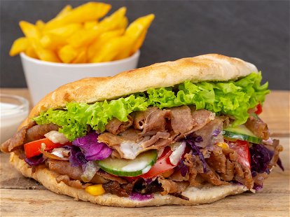 Döner Kebab Doner Kebap fast food in flatbread with fries on a wooden board panorama snack
