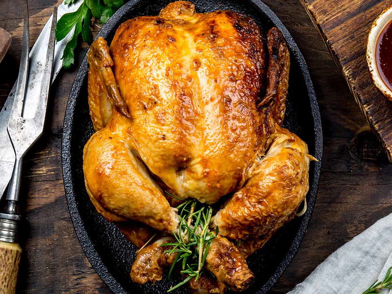 Roasted chicken with rosemary served on black plate with sauces on wooden table, top view