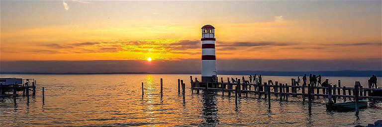 A majestic sunset on Lake Neusiedl enchants the sky with golden colours and is reflected in the calm waters. Nature in all its glory.