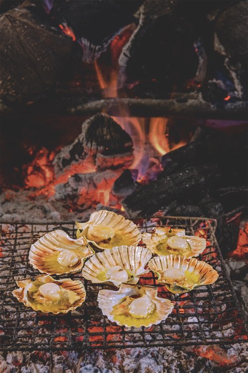 Jakobsmuscheln. 
Die Zubereitung über dem Feuer verleiht den Muscheln ein leicht rauchiges Aroma und macht das Fleisch ganz zart.