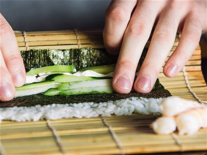 Chef rolling up sushi on a bamboo mat.