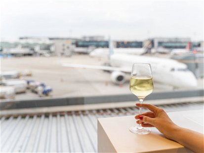 Female hand gently holding a glass of white wine in a cafe or restaurant with panoramic window with a view to an aircraft in an airport in Frankfurt. Travel and drink concept
