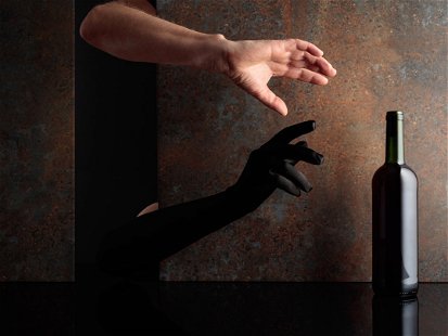Hands reach for a bottle of red wine. A concept image on the theme of expensive wines. Copy space.