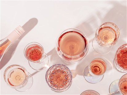 Many glasses of rose wine and bottle sparkling pink wine top view. Light alcohol drink for party. Flat lay on light table at summer day with shadows.