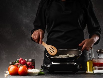 Frying onions, the chef cook in a pan on a background of vegetables. Culinary secrets and recipes. Restaurant and cafe business.