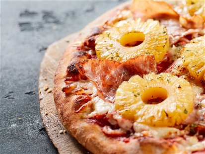 Tropical Hawaiian pizza with pineapple slices and ham on an oven-fired pastry base served whole on a board in a panorama banner with copyspace