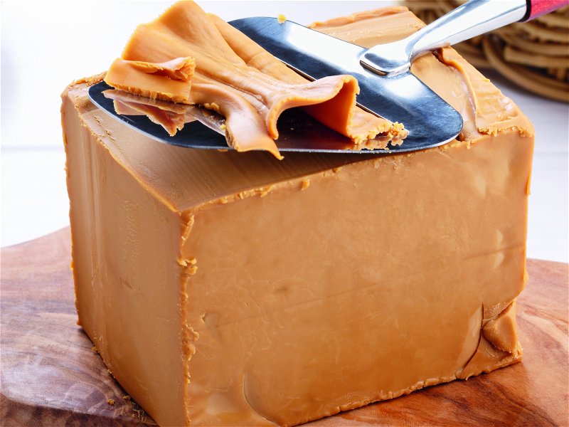 Die Farbe von Brunost kann von Karamell- bis Dunkelbraun variieren. Er wird in Blockform verkauft und mit einem Käsehobel in dünne Scheiben geschnitten.