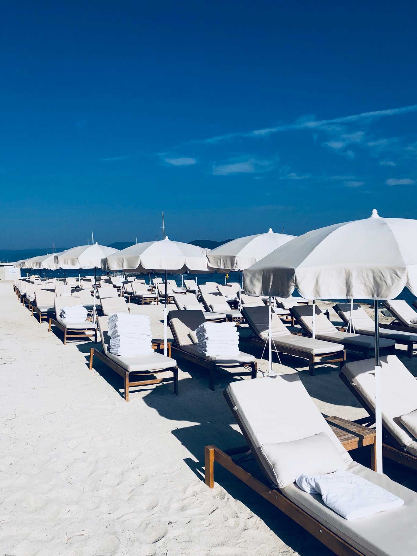 Die edlen weiß-braunen Sonnenliegen harmonieren herrlich mit dem hellen Sandstrand und dem blauen Himmel von St. Tropez. residencepinede.com