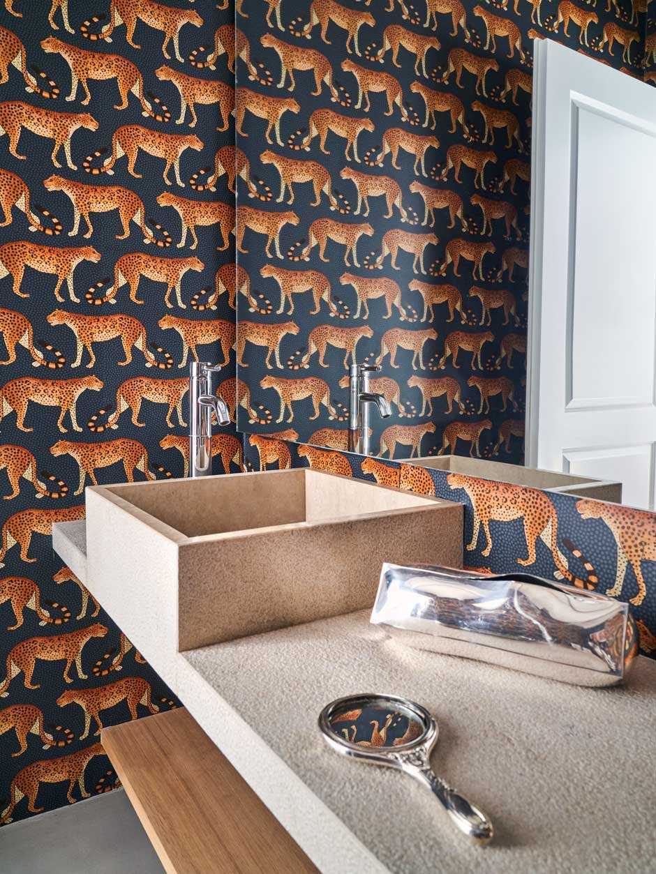 Tierisch Die Tapete mit Raubkatzenmotiv von Cole & Son belebt das Badezimmer samt Waschbecken aus Granit.
