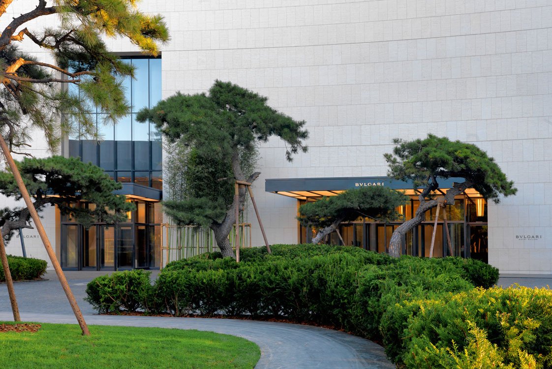 Mit sanfter Geste leitet Eneas Garten zum Eingang des »Bulgari Hotels« in Peking.